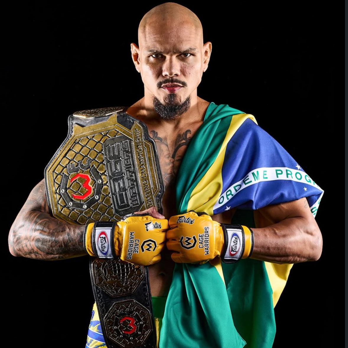 Man holding a championship belt with a Brazilian flag draped over his shoulder on a black background